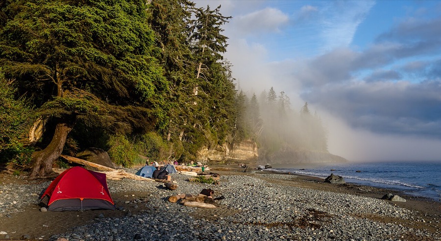 Tents on a driftwood-strewn gravel beach below coastal forest, Mystic Beach, Vancouver Island